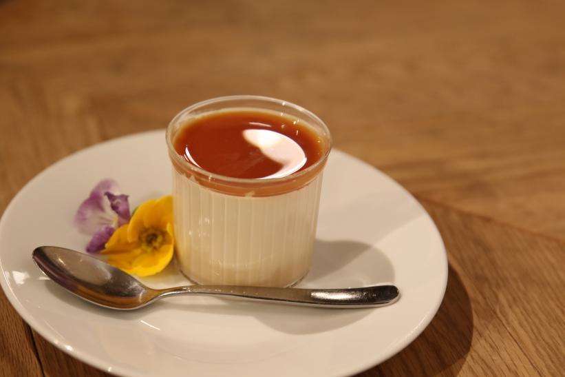 花弁とともに白いお皿に乗せられた透明な容器に入った紅茶のパンナコッタの写真