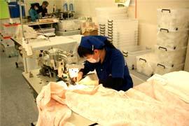 青い服を着た女性がミシンで布を縫っている写真