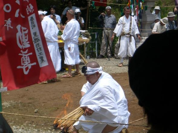 数人の人がいる前で一人の人が大量の木の棒に火をつけている火祭りの写真