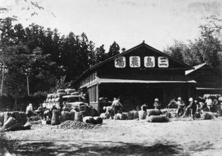 背の高い木の手前に右から書かれた「三嶋農場」の看板を掲げた木造の建物の白黒写真