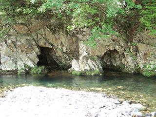 手前に川辺があり奥に穴がふたつある岩が見える写真