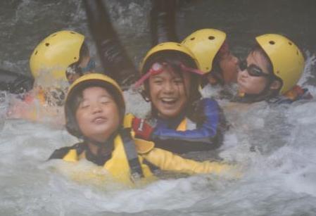水しぶきの中黄色いヘルメットを被った子どもたちが泳いでいる写真