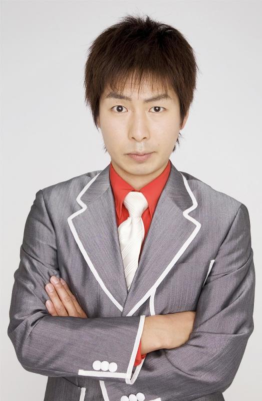 グレーのスーツにオレンジのシャツ、白いネクタイをあしらったU字工事の福田薫さんの写真