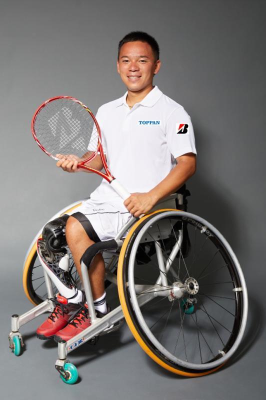 車椅子に乗ってテニスラケットを持ってはにかむ眞田卓さんの写真