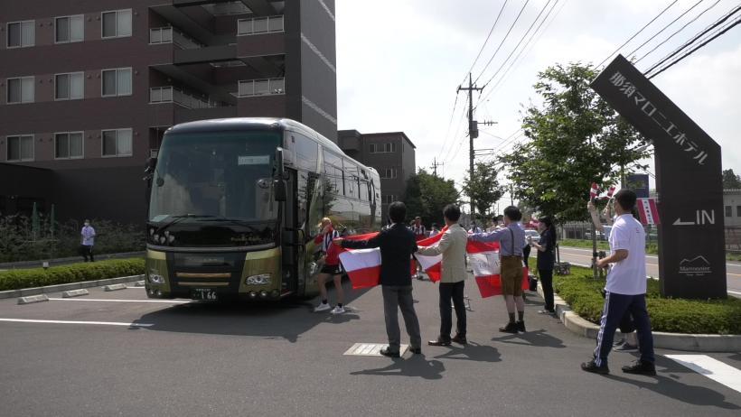 那須マロニエホテルの玄関前にて、選手村行きのバスに乗り込むオーストリア選手団の写真。バスの傍では日本側関係者たちが各々オーストリアの国旗を両手で掲げて見送る様子が確認できる