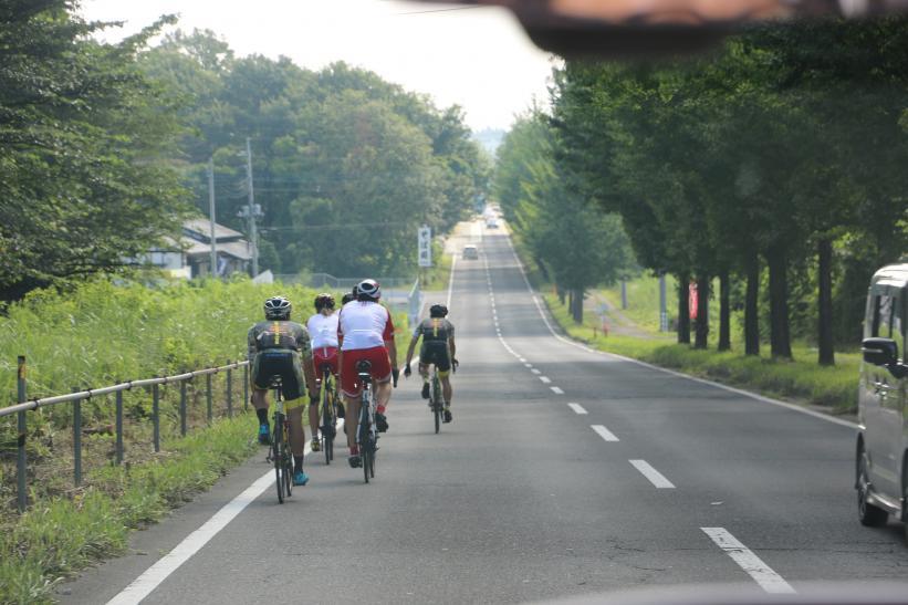 周囲に木々が繁る那須塩原市郊外の車道脇をロードバイクで走るオーストリアの選手たちの写真
