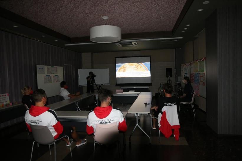 照明を落とした会議室で、スクリーンに映されたおもてなしメニュー開発の動画を鑑賞するオーストリアの選手たちの写真