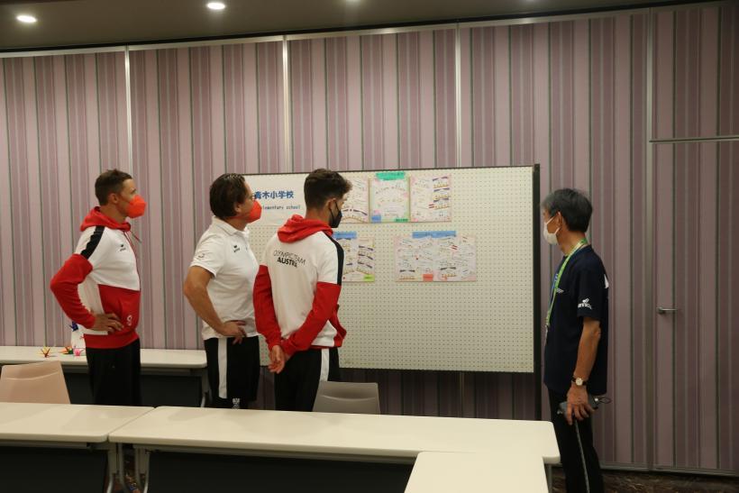 会議室にて市立青木小学校の児童からの応援メッセージが貼られたボードを見る、オーストリアの選手たちの写真